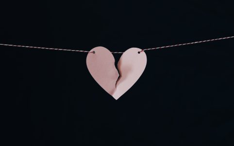 a pink paper heart ripped in the middle, hanging on a red and white striped wire against a black background
