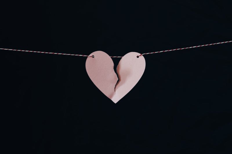 a pink paper heart ripped in the middle, hanging on a red and white striped wire against a black background