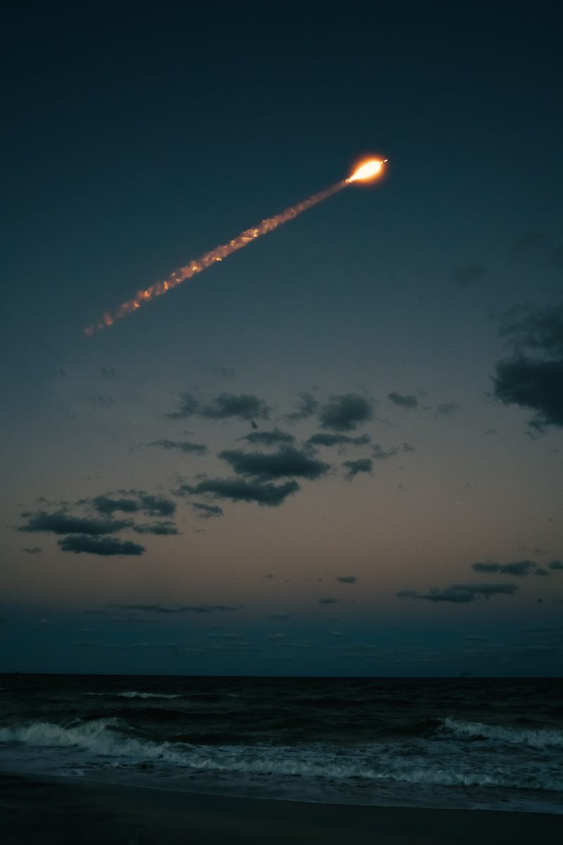 a rocket flies across the evening sky over an ocean, upward from left to right