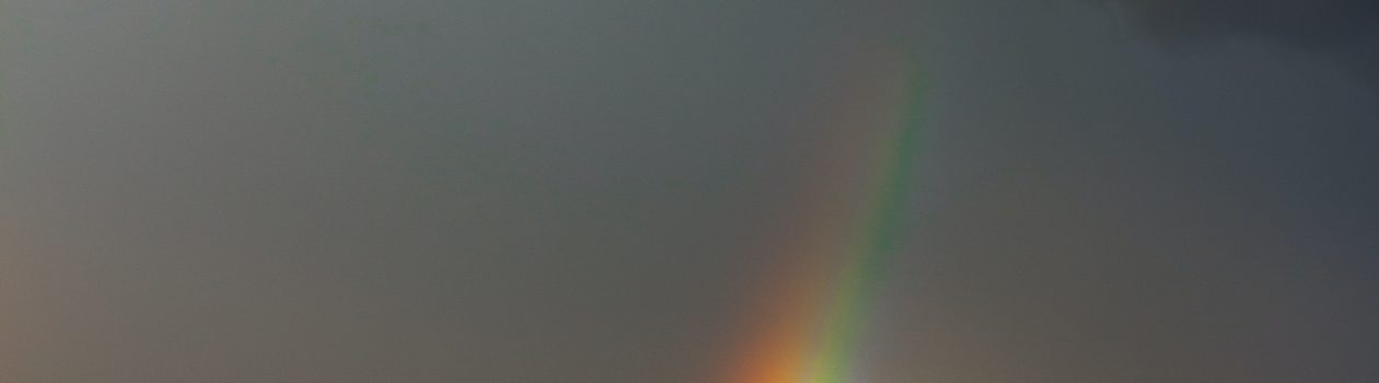 the end of a rainbow emerging from storm clouds over fields