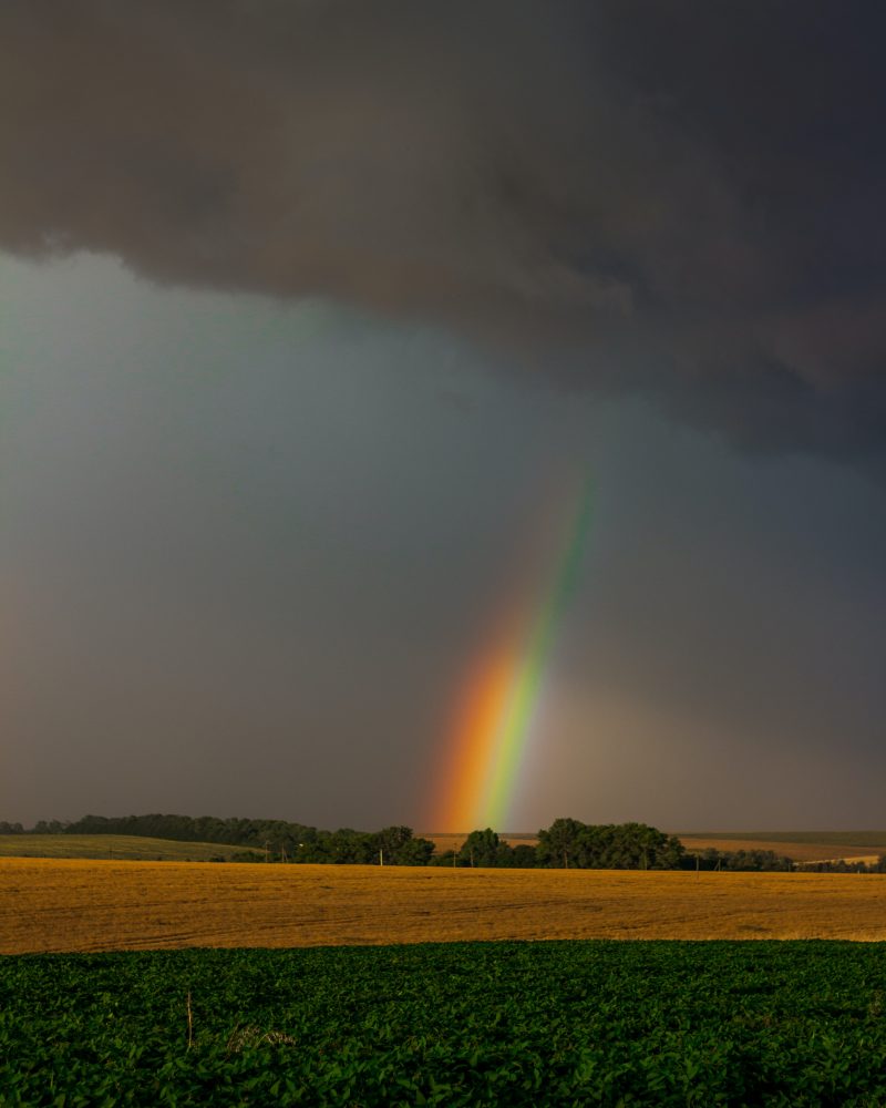 the end of a rainbow emerging from storm clouds over fields