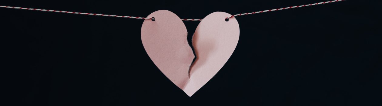 a pink paper heart ripped in the middle, hanging on a red and white striped wire against a black background