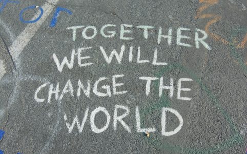 written in white chalk on pavement are the words 'TOGETHER WE WILL CHANGE THE WORLD'