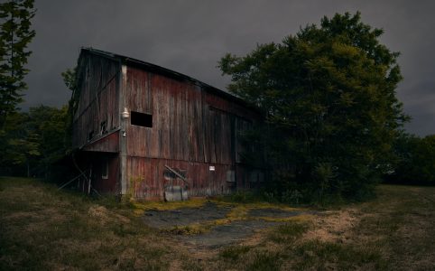 an old barn with fading red paint beside a large tree, against a midwest summer stormcloud background