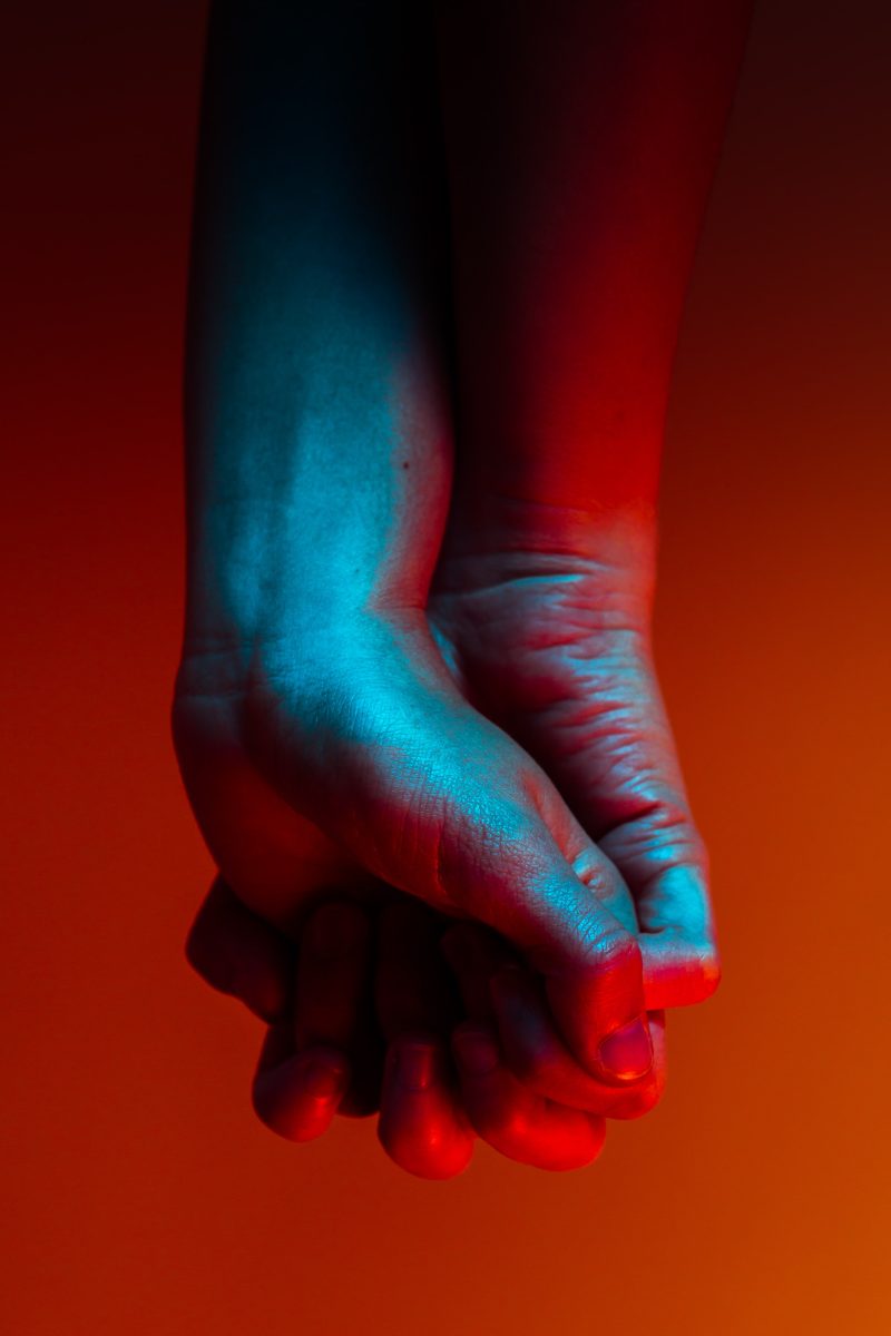 closeup of two people holding hands, palm outward, washed in blue light against a red background