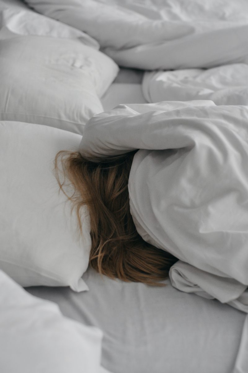 a person underneath white blankets with white pillows, with only light brown hair showing beneath the covers