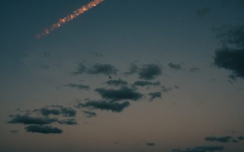 a rocket flies across the evening sky over an ocean, upward from left to right