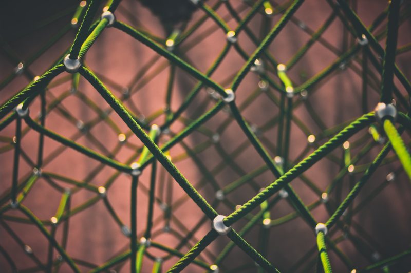 a three dimensional web of green rope against a clay colored background