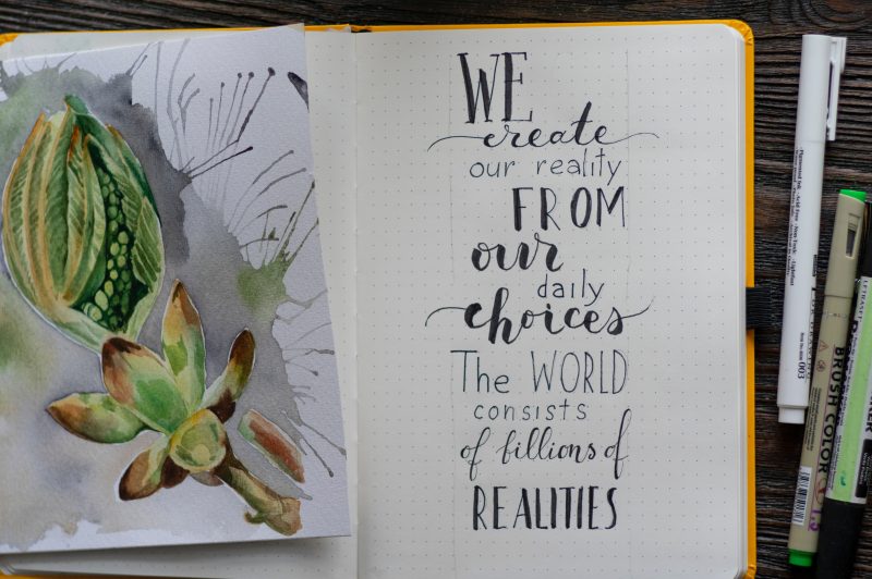 an open sketchbook with a watercolor flower bud on the left page, and the words 'We create our reality from our daily choices; the world consists of bills of realities."