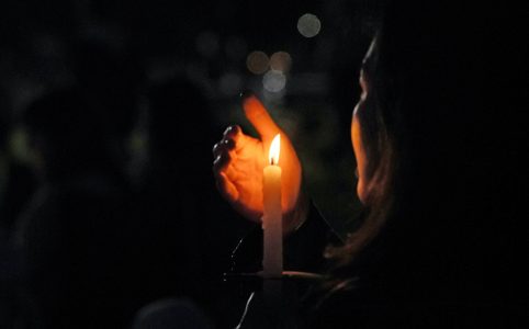 a person shields a candle's flame with their hand in the dark
