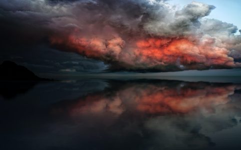 grey, black, and red lit clouds over a reflective lake surface