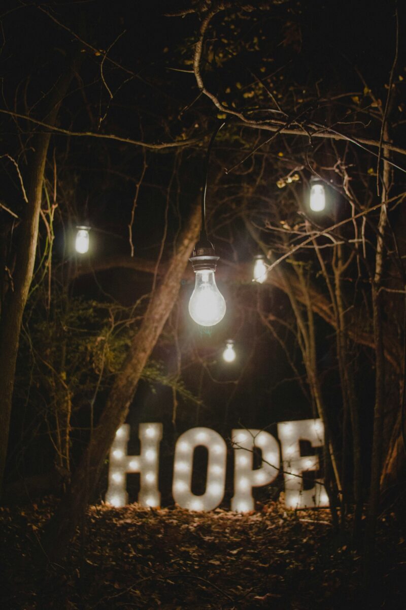 large letters made of lights that spell "HOPE" against a backdrop of trees and hanging lights at night